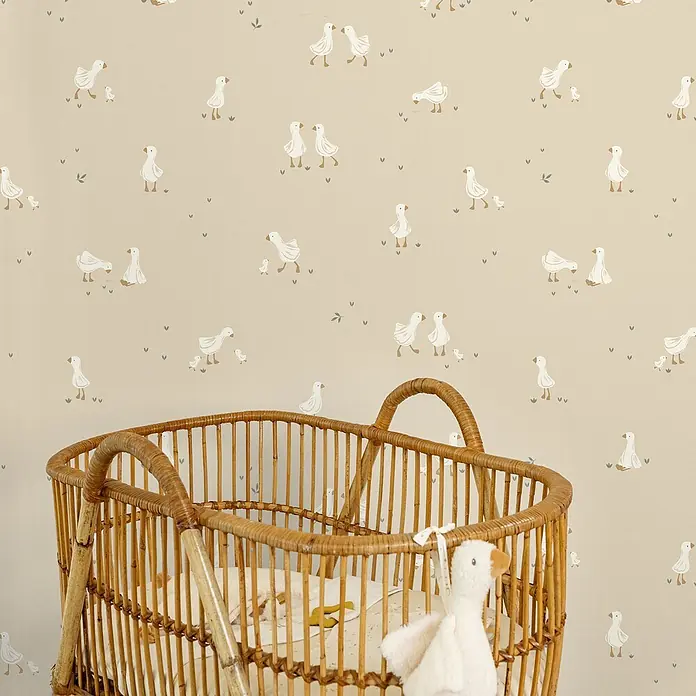 Little Dutch Vliestapete kleine Gans - Beige/Weiß, Tieroptik, 10 x 0,53 m - Natürliches Rattan-Babybett mit Plüschgans-Spielzeug vor einer Tapete mit Gänsemuster im Kinderzimmer.