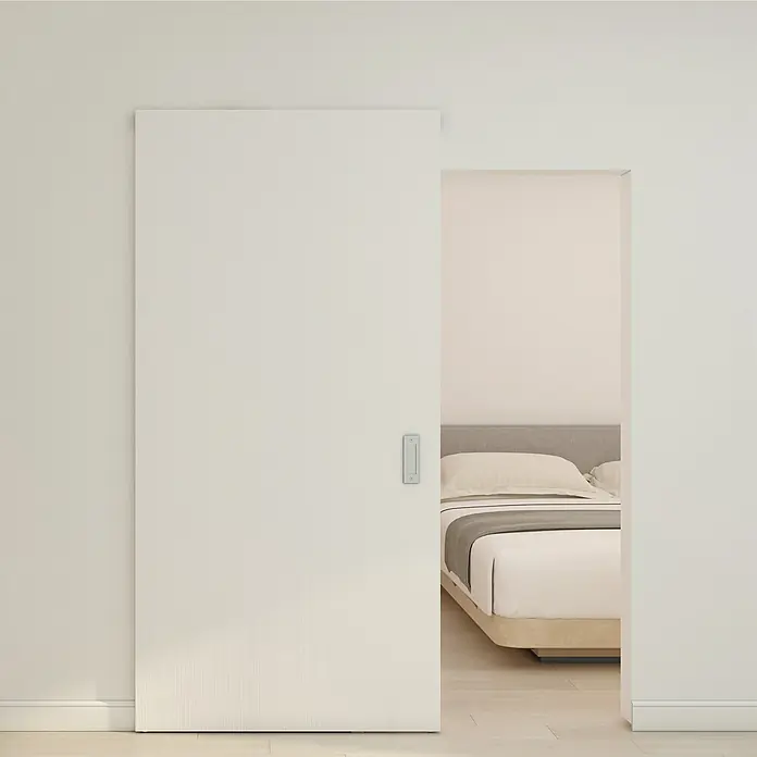 Inova Schiebetür-Komplettset Holzschiebetür Weiß mit verdeckter Laufschiene und Softclose 1030 x 2100 mm - 1.030 x 2.100 mm - Weiße texturierte Schiebetür mit eingelassenem Griff, teilweise geöffnet zu einem Schlafzimmer.