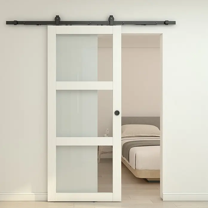 Inova Schiebetür-Komplettset Holzschiebetür Weiß mit Glaseinsatz und Softclose 900 x 2150 mm - 900 x 2.150 mm - Weiße Scheunentür mit Milchglas und schwarzer Schiebeschiene, teilweise geöffnet zu einem Schlafzimmer.