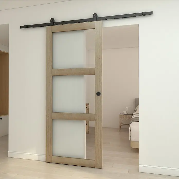 Inova Schiebetür-Komplettset Holzschiebetür Eiche mit Glaseinsatz und Softclose 900 x 2150 mm - 900 x 2.150 mm - Schiebetür im Scheunentor-Stil aus hellem Holz mit Milchglasscheiben, teilweise geöffnet an schwarzer Laufschiene, die zwei Räume verbindet.