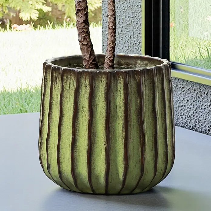 Hometopia Pflanztopf HTPL0078-GR - 1 Stk., Außenmaß (Ø x H): 23 x 21,5 cm, Keramik, Grün - Grüner geriffelter Keramik-Pflanztopf mit strukturierter Oberfläche und braunen Akzenten, mit zwei Pflanzenstämmen auf einer Terrasse.