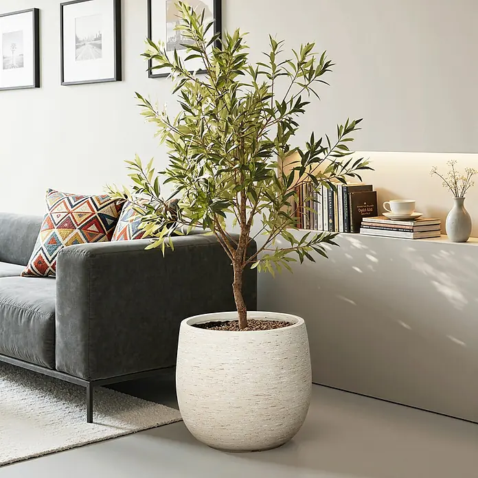 Hometopia Pflanztopf HTPL0166 - Außenmaß (Ø x H): 31 x 31,8 cm, Verbundwerkstoff, Weiß - Großer künstlicher Olivenbaum in einem strukturierten cremefarbenen Pflanzgefäß, neben einem grauen Sofa im Wohnzimmer.