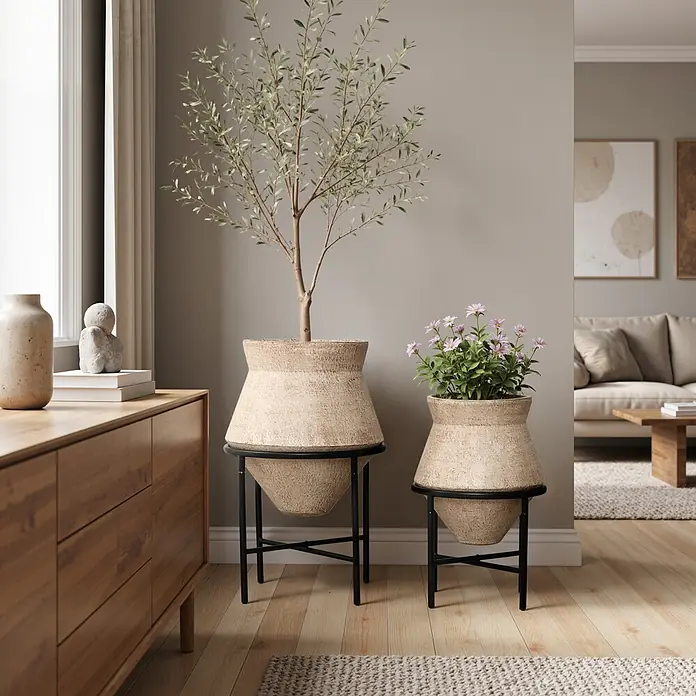 Hometopia Pflanztopf HTPL0359-BR - 2 Stk., Außenmaß (Ø x H): 62,5 x 62,5 cm, Metall, braun - Zwei strukturierte Pflanzgefäße auf schwarzen Metallständern im Wohnzimmer, das größere mit Baum, das kleinere mit Blumen.