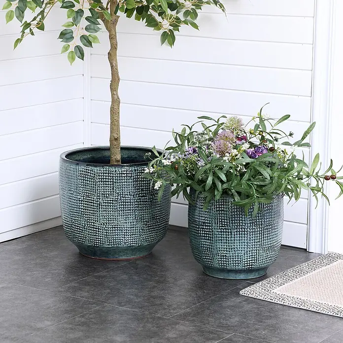 Hometopia Pflanztopf HTPL0037-L - 1 Stk., Außenmaß (Ø x H): 39 x 34 cm, Keramik - Zwei strukturierte, tealfarbene Keramik-Pflanzgefäße, eines mit einem Baum, das andere mit einem Blumenarrangement, auf dunklem Boden.