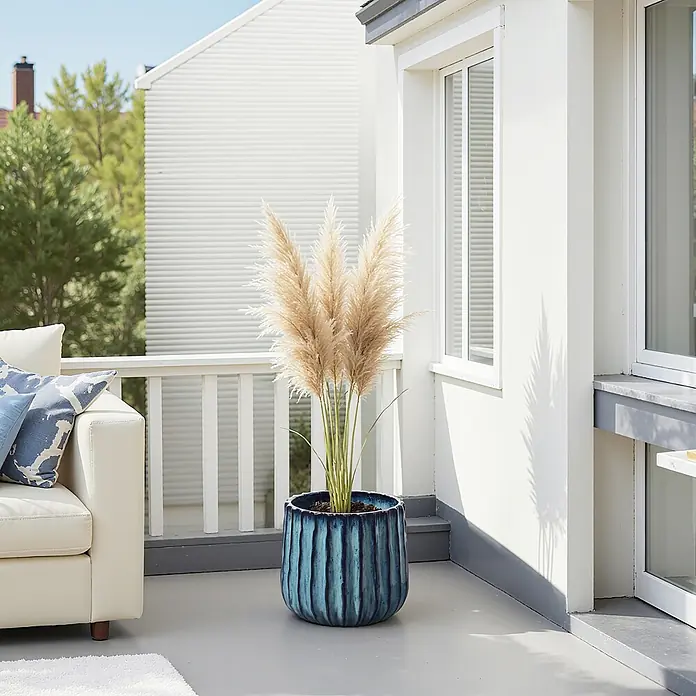 Keramik Blumentopf -  - Großer blauer, strukturierter Pflanzkübel mit hellem Pampasgras, auf einer Terrasse neben einem cremefarbenen Outdoor-Sofa.