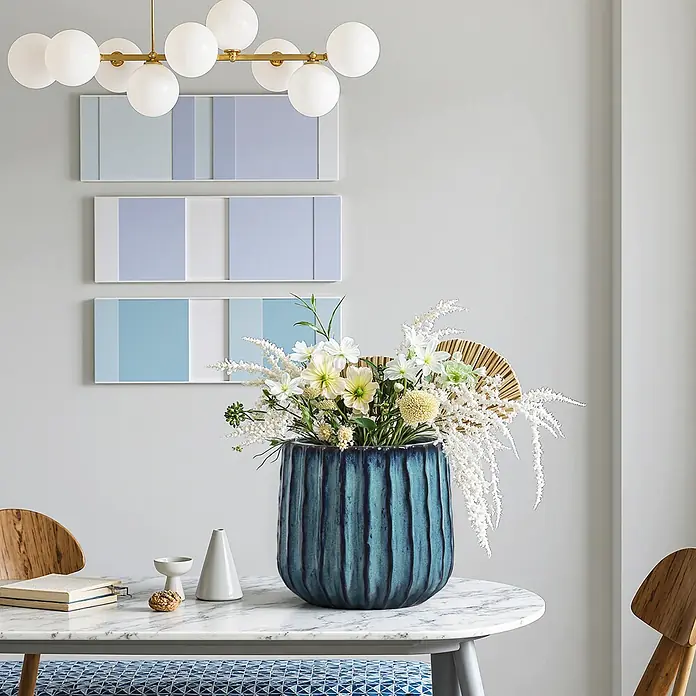 Keramik Blumentopf -  - Eine große blaue, strukturierte Vase mit weißen und gelben Blumen auf einem runden Marmortisch.