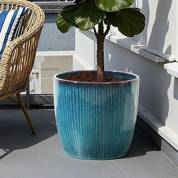 Hometopia Pflanztopf HTPL0081-M - 1 Stk., Außenmaß (Ø x H): 38 x 28,5 cm, Keramik, Blaugrün - Ein großer, gerippter, blaugrüner Keramikpflanztopf mit Pflanze steht auf einer Terrasse neben einem Korbstuhl.