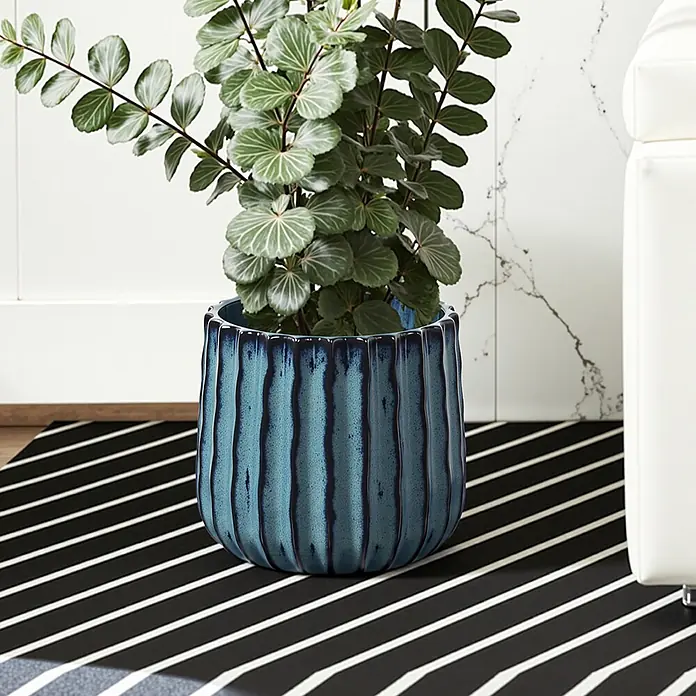 Keramik Blumentopf -  - Blauer, gerippter Keramik-Pflanztopf mit grüner Pflanze auf einem gestreiften Teppich.