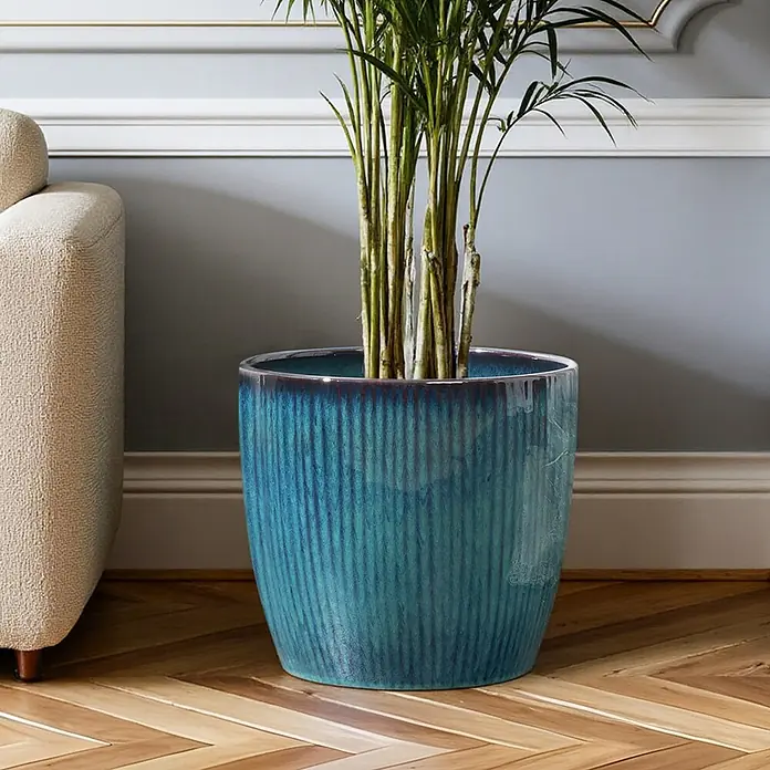 Hometopia Pflanztopf HTPL0081-M - 1 Stk., Außenmaß (Ø x H): 38 x 28,5 cm, Keramik, Blaugrün - Türkiser gerippter Keramik-Pflanztopf mit einer Grünpflanze auf Holzboden neben einem Sofa.