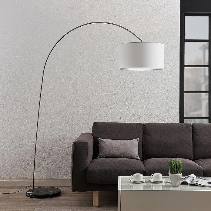 Lindby Stehlampe in nickel satiniert, weiß, Bogenlampe Wohnzimmer -  - Silberne Bogenstehleuchte mit weißem Trommelschirm und schwarzem Marmorfuß, neben einem dunkelgrauen Sofa.