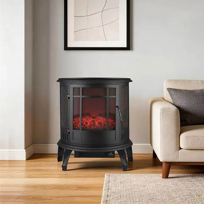 Chimenea eléctrica Tambora - 29 x 56 x 63,5 cm, Negro - Chimenea eléctrica negra con puerta de malla y llamas artificiales, junto a un sofá beige en una sala de estar.