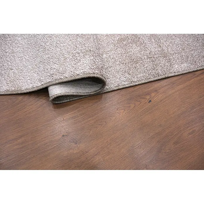 Alfombra de pelo corto Bicolor - Natural, 200 x 140 cm, 100% poliéster - Una alfombra de textura beige claro está parcialmente enrollada, revelando su reverso, sobre un suelo de madera marrón cálido.