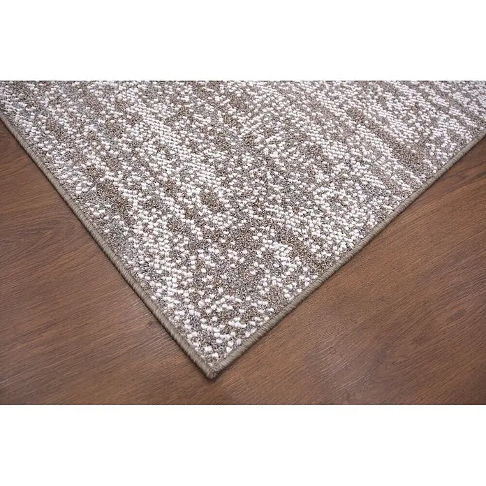 Alfombra de pelo corto Loop - Natural, 230 x 160 cm, 100% poliéster - Primer plano de una alfombra gris y blanca moteada con borde unido, sobre un suelo de madera oscura.
