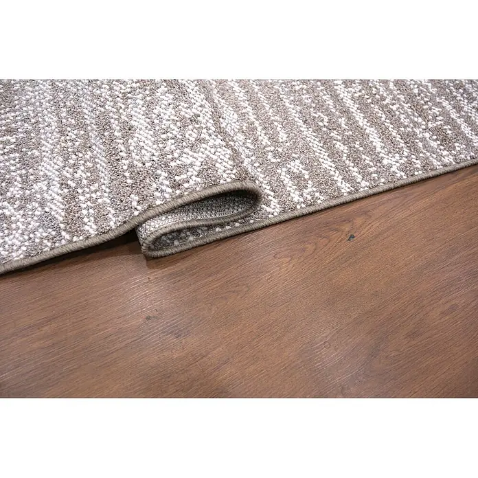 Alfombra de pelo corto Loop - Natural, 230 x 160 cm, 100% poliéster - Una alfombra de patrón beige y blanco, parcialmente enrollada, sobre un suelo de madera.