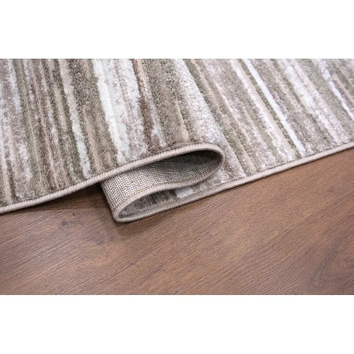 Alfombra de pelo corto Triple Columna - Verde, 200 x 140 cm, 100% poliéster - Alfombra rayada texturizada en beige, marrón y blanco, parcialmente enrollada en suelo de madera, mostrando su borde y reverso.