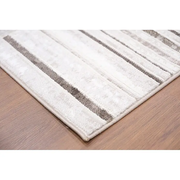Alfombra de pelo corto Box - Natural, 230 x 160 cm, 100% poliéster - Primer plano de una alfombra suave de color claro con rayas marrones gruesas, colocada sobre un suelo de madera cálido.