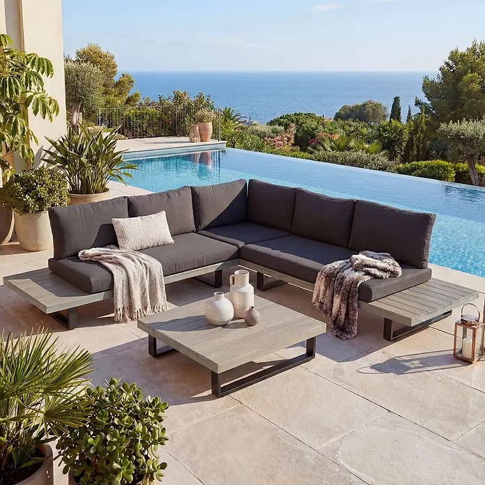 Mendler Loungemöbel-Set HWC-H54 - 2 -tlg., Holz, Grau, Polster dunkelgrau, Grau, Polster dunkelgrau - Outdoor-Ecksofa mit dunkelgrauen Kissen und hellgrauem Lattenrost, dazu passender Couchtisch, auf einer Terrasse.