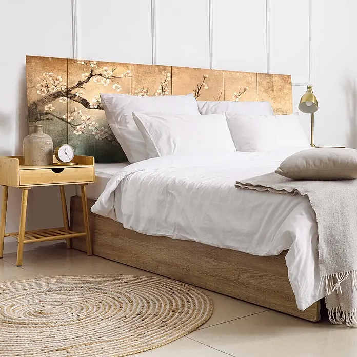 Cabecero de cama Hanami - L x An: 115 x 60 cm, Natural - Cabecero de madera con diseño de flor de cerezo detrás de una cama con ropa blanca, una mesita de noche y una alfombra trenada.