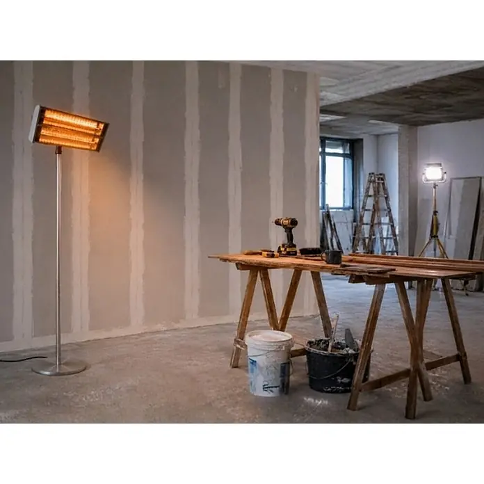 WDH Heizlüfter WDH-240GT Standheizstrahler, Edelstahl mit goldenen Heizröhren - 2,4 kW, Silber, IP55 - Silberner Stand-Infrarotstrahler mit leuchtenden orangefarbenen Heizlampen, der in einem Baubereich Wärme spendet.