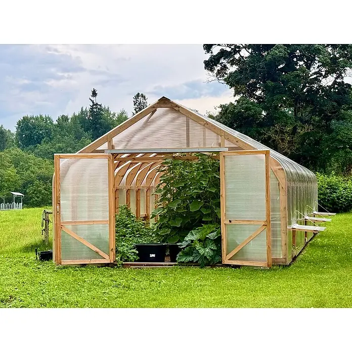 Garten Dream Gewächshaus Classic Wood - 450 x 800 cm, Material Seitenwand: Kunststoff, 10 mm, Braun - Ein Gewächshaus mit Holzrahmen und transluzenten Paneelen, gefüllt mit grünen Pflanzen, in einer Graslandschaft.