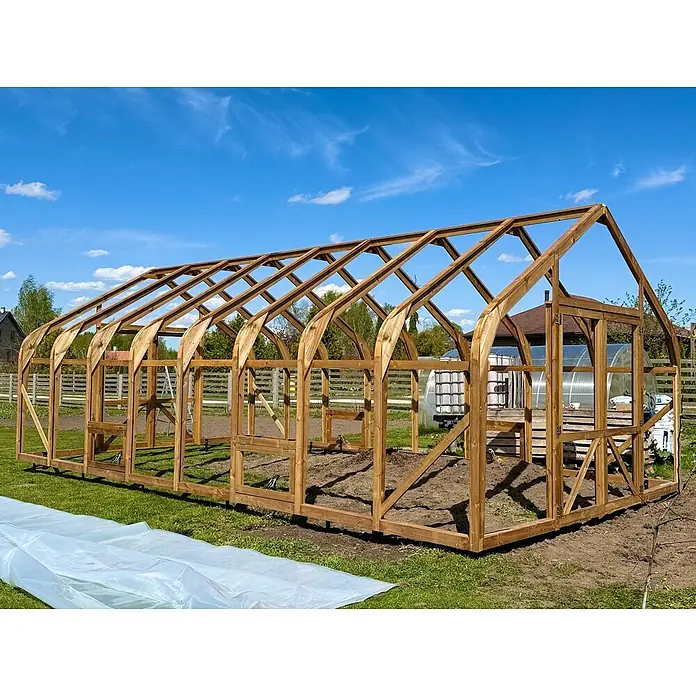 Garten Dream Gewächshaus Classic Wood - 450 x 800 cm, Material Seitenwand: Kunststoff, 10 mm, Braun - Brauner Holzgewächshausrahmen im Bau in einem sonnigen Garten, mit Erde und Plastikfolie auf dem Gras.
