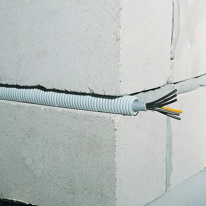 Flexrohr EN16 - Beton, 25 m, Kunststoff, 320 N, Grau, 16 mm - Detailaufnahme eines grauen Elektroinstallationsrohrs mit freiliegenden Kabeln, das zwischen grauen Betonblöcken verläuft.