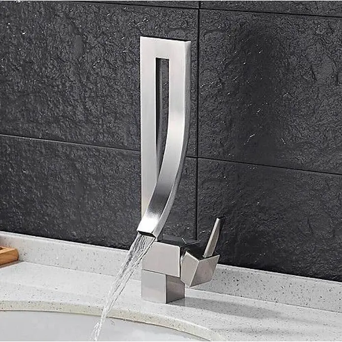 Hudor Waschtischarmatur Enipée 005 - Hochglänzend - Moderner Wasserfallhahn aus gebürstetem Metall mit geschwungenem Design, aktiv Wasser in ein Waschbecken leitend, an dunkler Texturwand montiert.