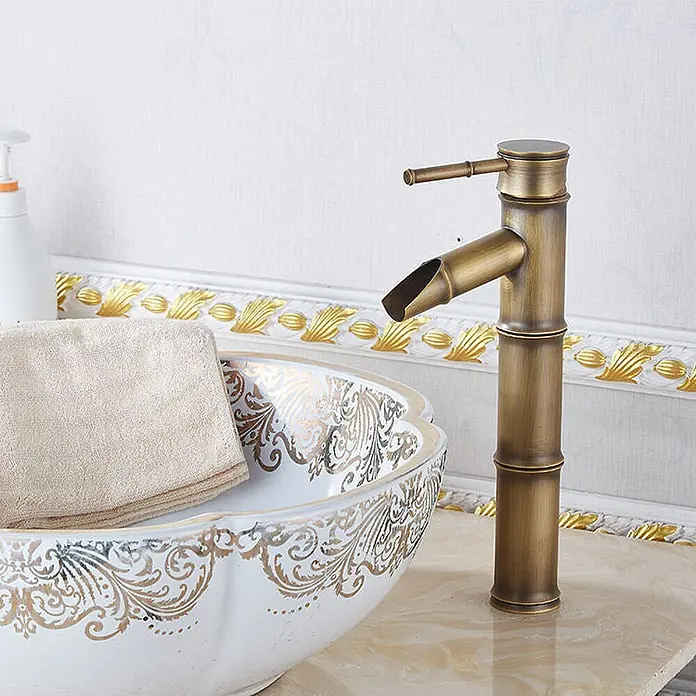 Hudor Waschtischarmatur Artémis 7833 - Seidenmatt - Messingfarbener Wasserhahn in Bambusform neben einem weiß-goldenen Waschbecken.