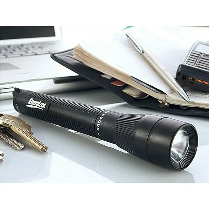 Energizer Linterna X-Focus - 9 lm, IP44 - La imagen muestra una linterna Energizer negra con función de enfoque sobre un escritorio, junto con otros artículos de oficina.