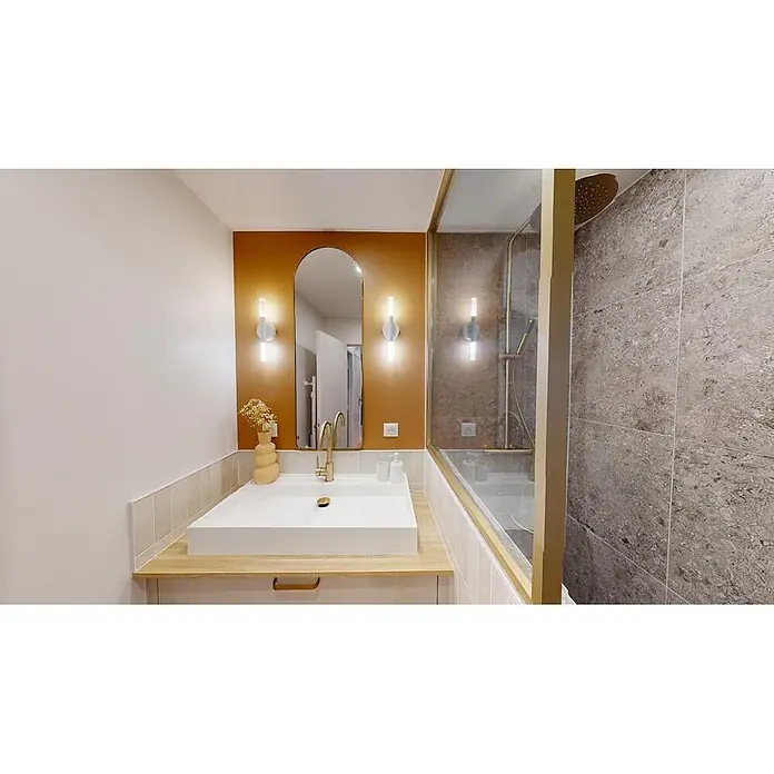 Hudor Waschtischarmatur Scamandre 6565 - Seidenmatt - Modernes Badezimmer mit orangefarbener Akzentwand, weißem Waschbecken, goldenen Armaturen und Dusche mit grauen Fliesen.