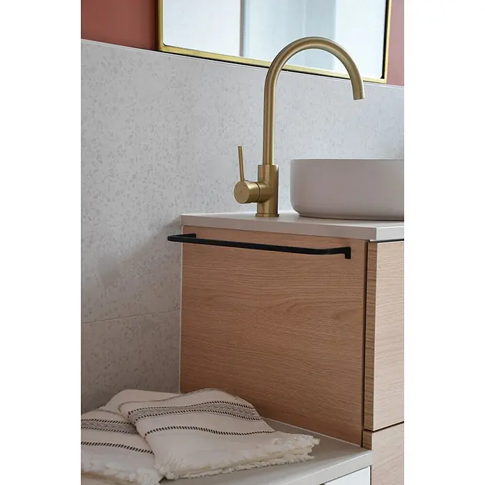 Hudor Waschtischarmatur Scamandre 6565 - Seidenmatt - Moderner Waschtisch mit goldener Armatur, weißem Aufsatzwaschbecken und hellem Holzschrank mit schwarzem Handtuchhalter. Ein gestreiftes Handtuch liegt unten.