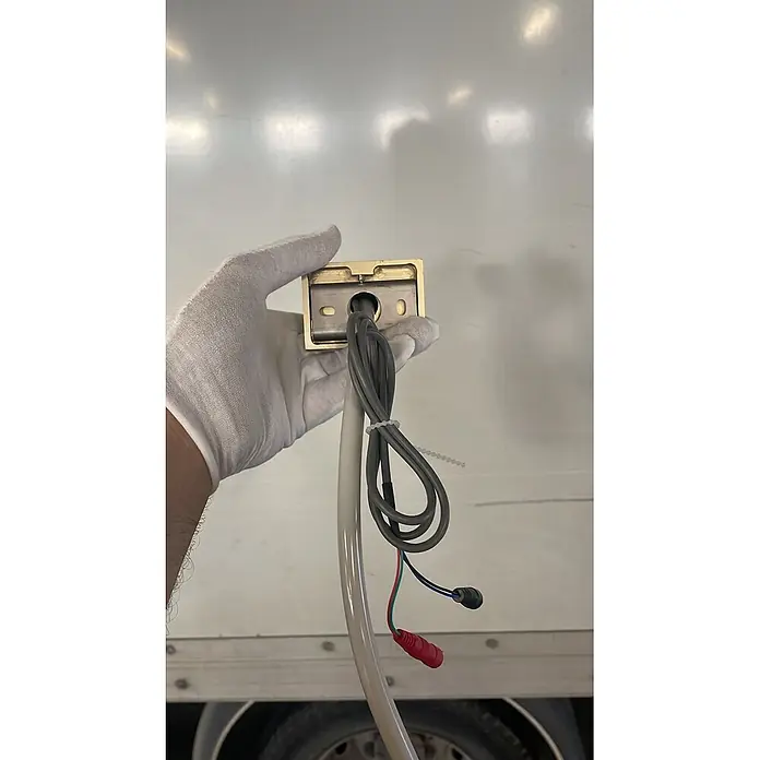 Hudor Waschtischarmatur 018 - Hochglänzend - Messingfarbenes rechteckiges Gerät mit grauem Kabel und roten sowie blauen elektrischen Anschlüssen, gehalten von einer behandschuhten Hand.