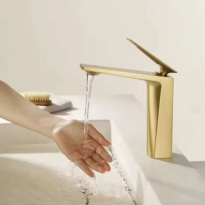 Hudor Waschtischarmatur Scamandre 7697 - Seidenmatt - Goldfarbener moderner Wasserhahn im Waschbecken, Wasser fließt über eine Hand.