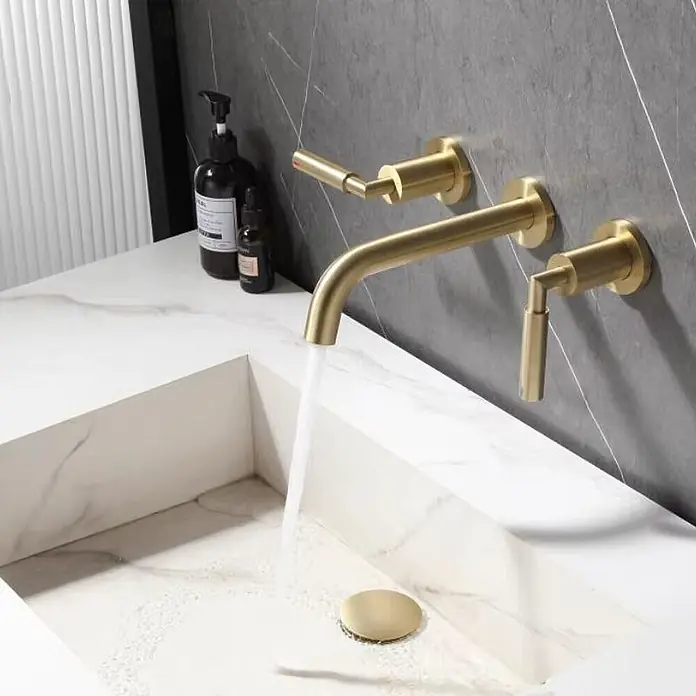 Hudor Waschtischarmatur 7864 - Seidenmatt - Wandmontierter Wasserhahn aus gebürstetem Gold mit separaten Griffen, Wasser fließt in ein weißes Marmorwaschbecken mit passendem Goldabfluss.