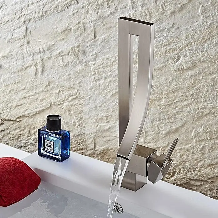 Hudor Waschtischarmatur - Seidenmatt - Moderner Wasserhahn aus gebürstetem Metall mit einzigartigem Design, Wasser fließt in ein weißes Waschbecken; daneben Parfüm und ein Handtuch.