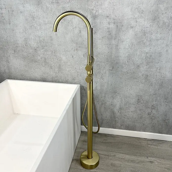 Hudor Badewannenarmatur Scamandre 007 - Seidenmatt - Freistehende Badewannenarmatur in gebürstetem Gold mit gebogenem Auslauf, Bedienknöpfen und integrierter Handbrause, neben einer weißen Wanne.
