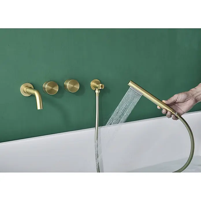 Hudor Badewannenarmatur Scamandre 078 - Seidenmatt - Gebürstete Messing-Wannenarmatur und Handbrause, Wasser in eine weiße Wanne gießend, von einer Hand gehalten.