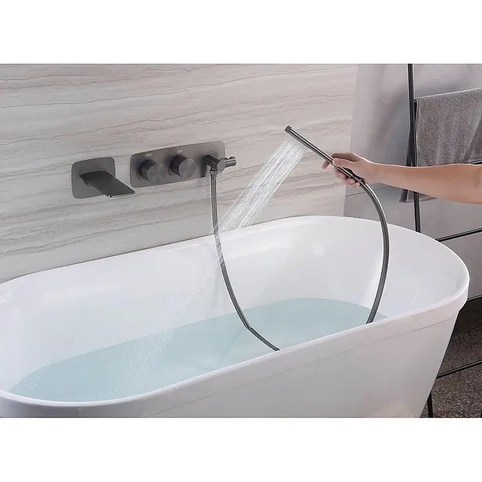 Hudor Badewannenarmatur 088 - Seidenmatt - Dunkelgraue wandmontierte Badewannenarmatur mit Handbrause, die Wasser in eine weiße Wanne sprüht, von einer Hand gehalten.