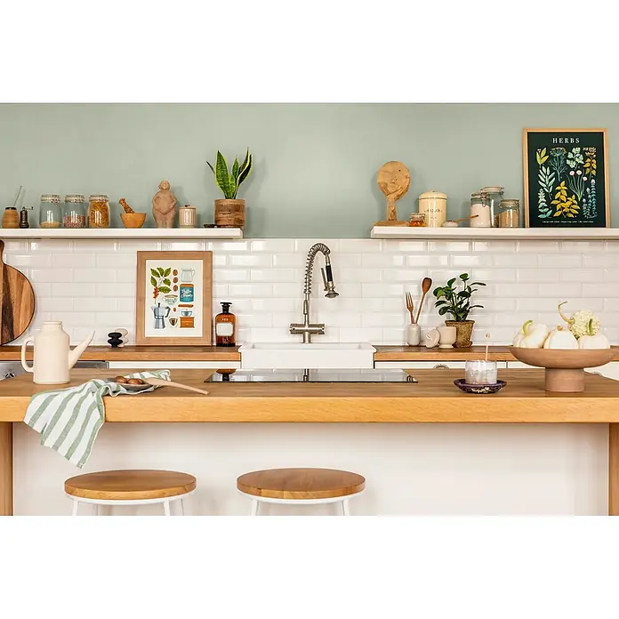 Caleo Color Wandfarbe Lehmfarbe Jade - Jade, Matt, 10 l - Moderne Küche mit weißen Fliesen, Arbeitsplatten aus Holz und Regalen mit Gläsern, Pflanzen und Bildern.