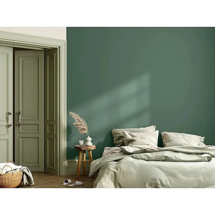Caleo Color Wandfarbe Lehmfarbe Feigenblatt - Feigenblatt, Matt, 0,15 l - Ruhiges Schlafzimmer mit weicher hellgrüner Bettwäsche auf einem Bett vor einer dunkelgrünen Wand.
