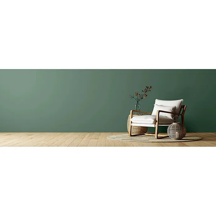 Caleo Color Wandfarbe Lehmfarbe Feigenblatt - Feigenblatt, Matt, 0,15 l - Ein moderner Sessel mit hellem Holzrahmen und weißen Kissen, daneben ein Weidenkorb, Vase mit Ästen und eine Weidenlaterne, auf Holzboden.