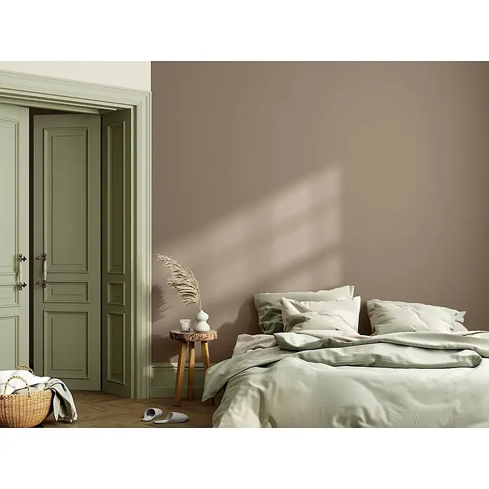 Caleo Color Wandfarbe Lehmfarbe Steineiche - Steineiche, Matt, 0,15 l - Weiche, hellgrüne Bettwäsche bedeckt ein Bett in einem ruhigen Schlafzimmer.