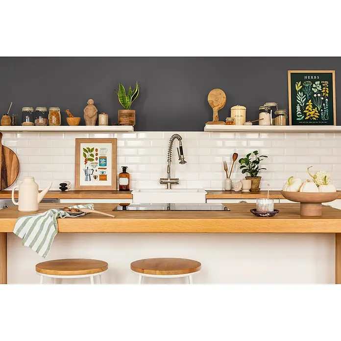 Caleo Color Wandfarbe Lehmfarbe Ebenholz - Ebenholz, Matt, 0,15 l - Eine helle Kücheninsel aus Holz mit integriertem Spülbecken und Kochfeld, darunter zwei weiße Barhocker.