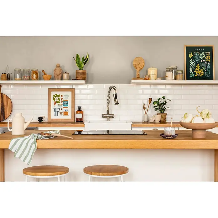 Caleo Color Wandfarbe Lehmfarbe Sanddüne - Sanddüne, Matt, 10 l - Eine modern-rustikale Küche mit hellen Holztheken, weißen Metrofliesen, offenen Regalen mit Gläsern und Deko, Spüle und Barhockern, die einen warmen, organisierten Raum schaffen.