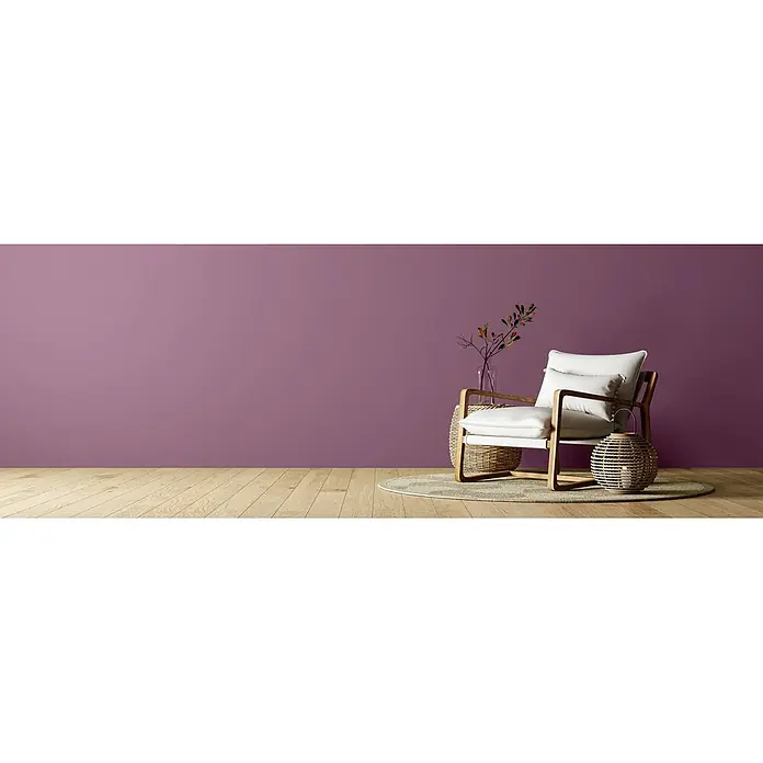 Caleo Color Wandfarbe Lehmfarbe Heidekraut - Heidekraut, Matt, 2,25 l - Beiger Sessel mit Holzrahmen auf rundem Teppich vor violetter Wand und Holzboden, mit Deko-Elementen.