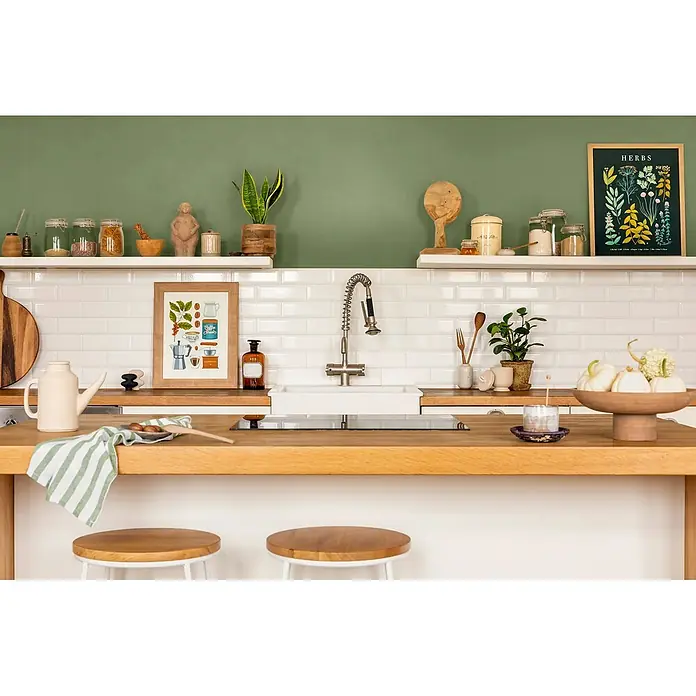 Caleo Color Wandfarbe Lehmfarbe Weideland - Weideland, Matt, 2,25 l - Eine Küche mit warmer Holztheke, weißem Fliesenspiegel und grüner Wand. Dekoriert mit Pflanzen, Utensilien und Küchenutensilien.