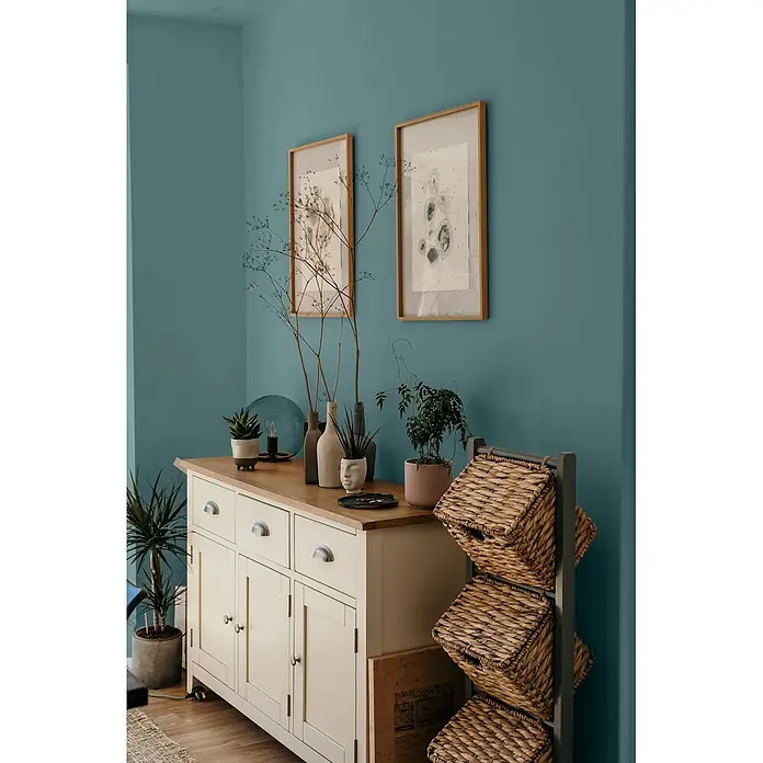 Caleo Color Wandfarbe Lehmfarbe Bergsee - Bergsee, Matt, 0,15 l - Cremefarbenes Sideboard mit heller Holzplatte und Korbregal in einem tealfarbenen Raum.