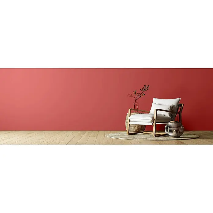 Caleo Color Wandfarbe Lehmfarbe Mohnblume - Mohnblume, Matt, 2,25 l - Moderner Sessel mit hellem Holzrahmen und weißen Polstern in einem Raum mit roter Wand. Verziert mit einer Vase und einer geflochtenen Laterne.