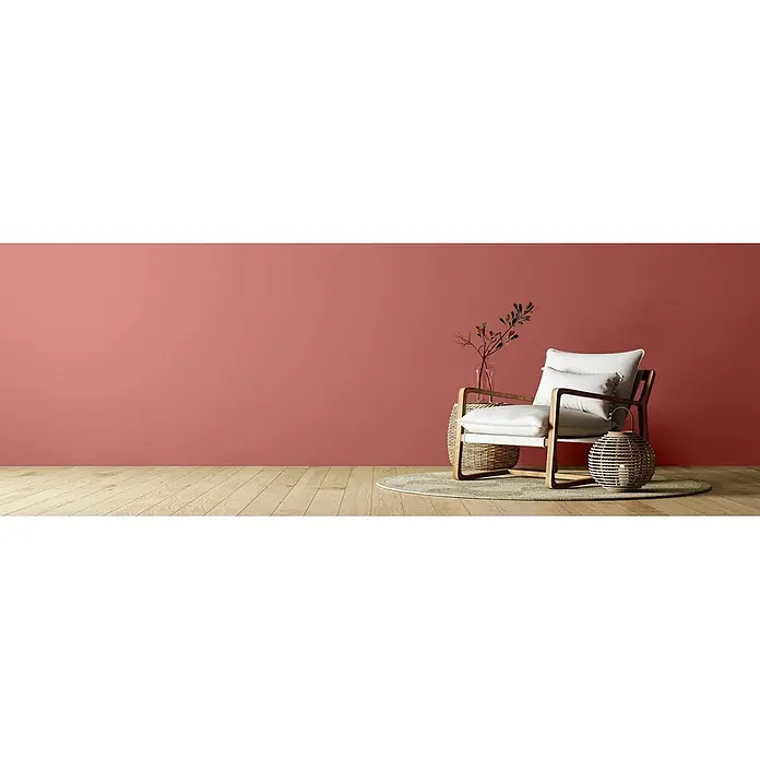Caleo Color Wandfarbe Lehmfarbe Rosenknospe - Rosenknospe, Matt, 5 l - Ein moderner Sessel mit hellem Holzrahmen und weißen Polstern, auf einem runden Teppich in einem korallfarbenen Raum mit Holzfußboden.