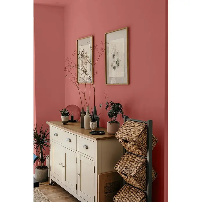 Caleo Color Wandfarbe Lehmfarbe Rosenknospe - Rosenknospe, Matt, 5 l - Cremefarbenes Sideboard mit Holzplatte und Pflanzen, daneben ein dunkelgraues Regal mit drei geflochtenen Weidenkörben.